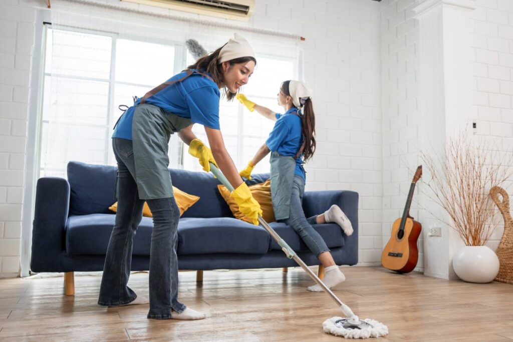Asian young woman cleaner team cleaning indoors in living room at home. Two beautiful girl housewife housekeeper cleaner feeling happy and relax, enjoy housekeeping housework or chores in house.