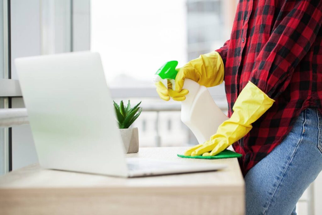 Young Happy Female Janitor Cleaning Wooden Desk With Rag In Office.